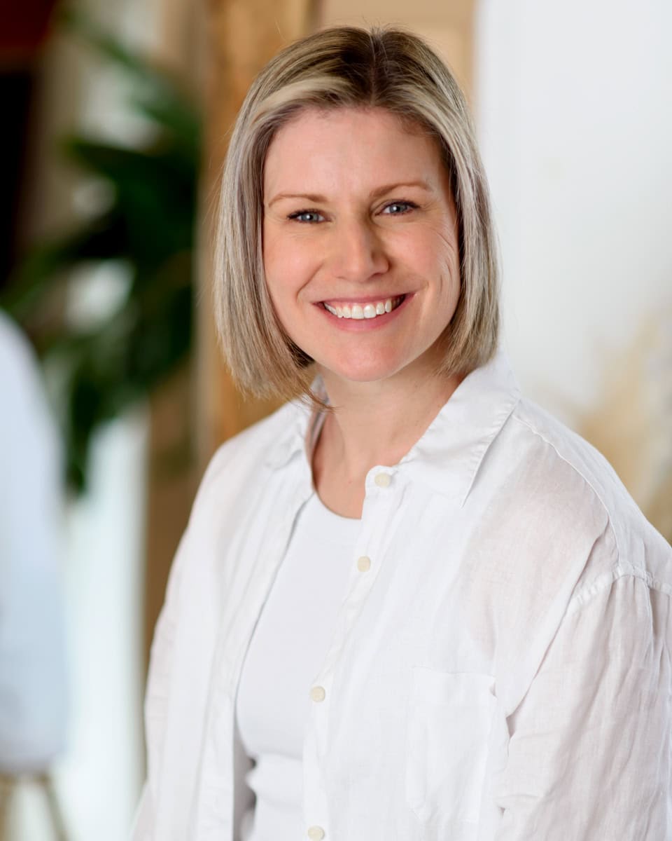 Karinne Faddy from Resonates within Holistic coaching wears a white shirt and smiles looking happy and relaxed. Brand photo taken by Molly Rhianon Photography.