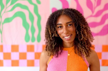 a brans photo of Nina robinson staNDING IN FRONT OF A COLOURFUL PINK AND GREEN BACKGROUND SMILING AND LIIKING AT THE CAMERA. SHE HAS AFRO HAIR AND LOOKS RELAXED