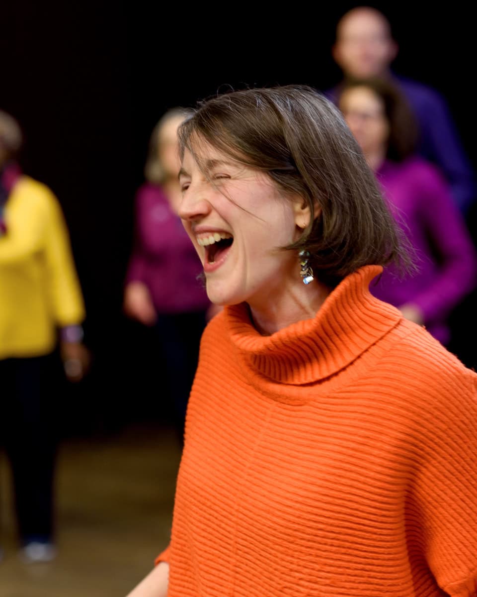 a joyful photo of Eleanor rastell from palace acapella choir in Crystal Palace. Choir members wear multi coloured clothes in block colours during their rehearsal photographed by Molly Rhianon Photography