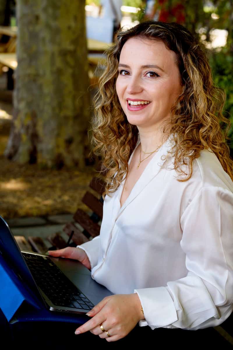 a personal branding photo of a female business owner sitting on a bench smiling naturally wearing a white shirt and gold accessories. Photo by Molly Rhianon Photography